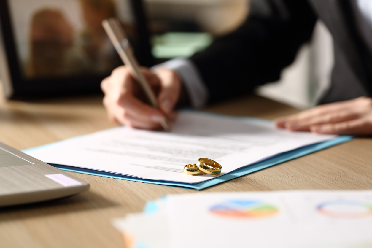Man signing divorce papers with wedding rings in foreground