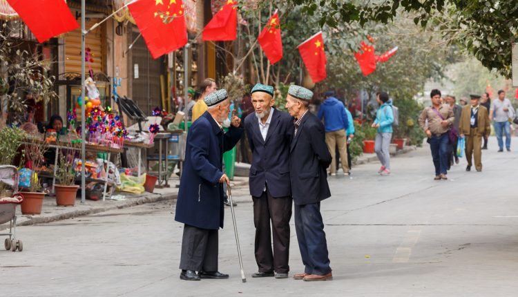 Three elderly Uighur men having a conversation in front of Chinese flags