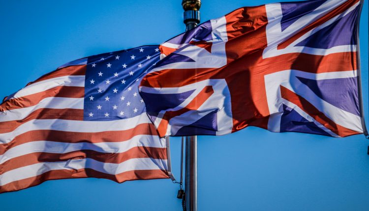 US and UK flag against blue sky