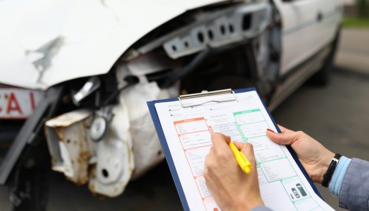 Insurance agent holds clipboard and ballpoint pen closeup and wrecked car in background. Vehicle insurance concept.