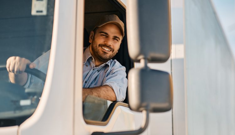 Happy professional truck driver driving his truck and looking at camera. Copy space.