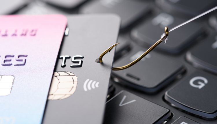 Credit card on fishing hook pulled from stack on keyboard, phishing scam data theft concept