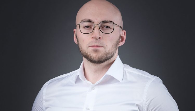 Marketing specialist Shamil Shamilov standing in front of a dark background.