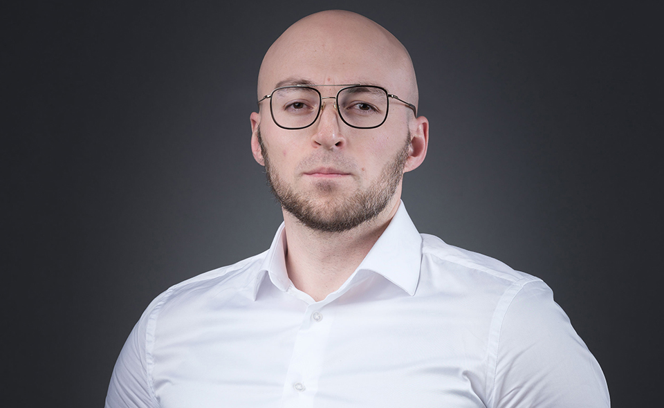 Marketing specialist Shamil Shamilov standing in front of a dark background.