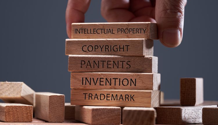man adding a block showing the words Intellectual property on top of other wooden block with text copyright, patents, invention,and trademark