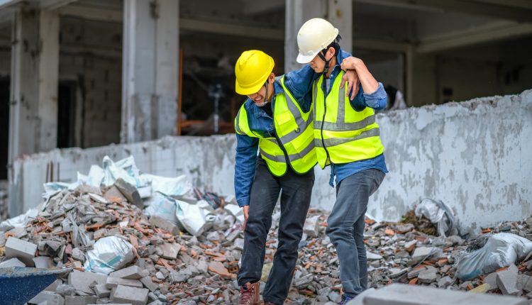 Construction supervisors or engineers help construction workers who have knee and leg injuries, caused by accidents at the construction site.