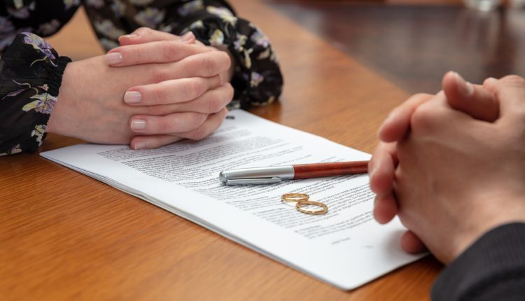 Signing a divorce, marriage dissolution documents and agreement. Wife and husband hands, wedding rings and legal papers for signature on a wooden table, lawyer office