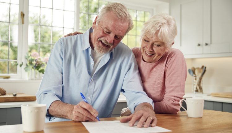 Retired Senior Couple Sitting In Kitchen At Home Signing Financial Document