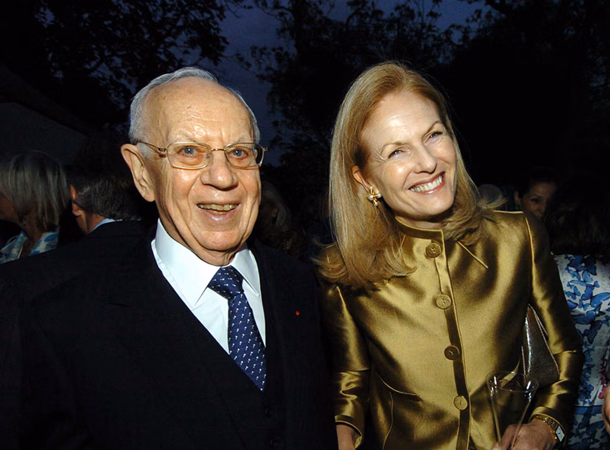 Mortimer Sackler smiling alongside a woman at an evening event, both dressed formally and surrounded by other guests.