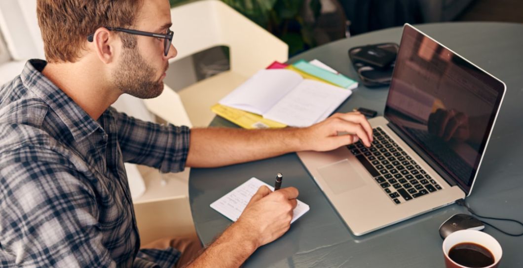 man using a laptop and writing notes