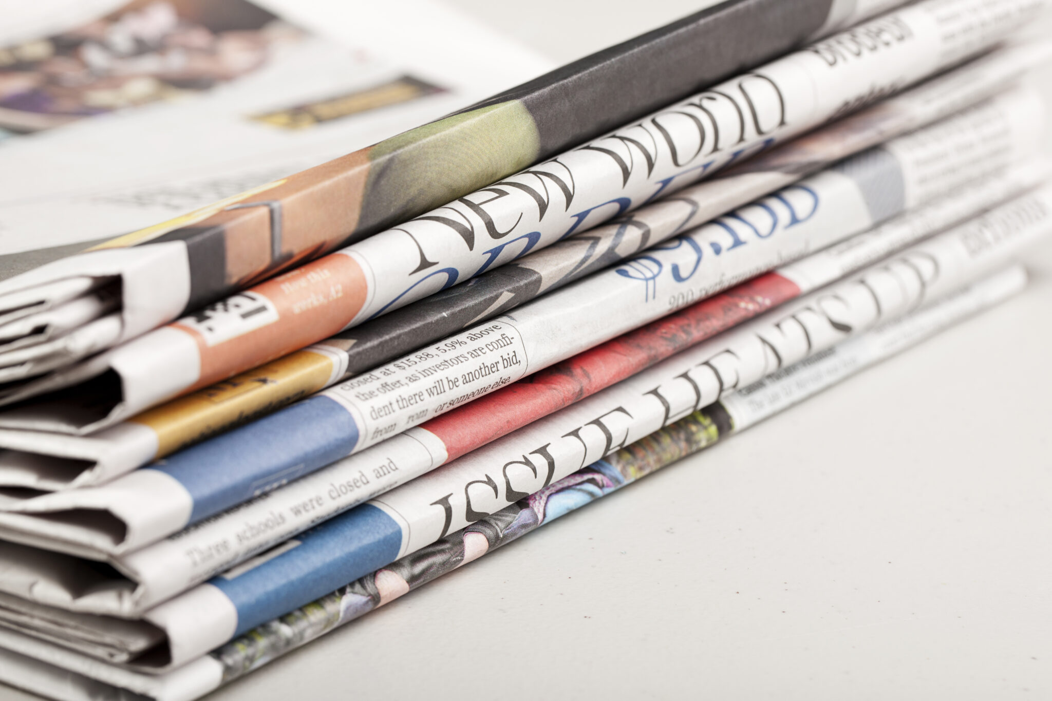 A stack of folded newspapers featuring colorful front pages and visible headlines, representing print media and journalism.