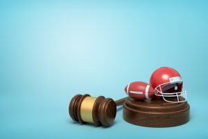 3d rendering of ball and helmet for american football on sounding block with judge gavel lying beside on light blue background.