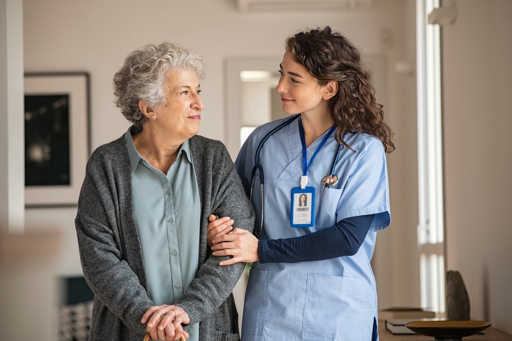home caregiver supporting senior woman in her house, holding hands