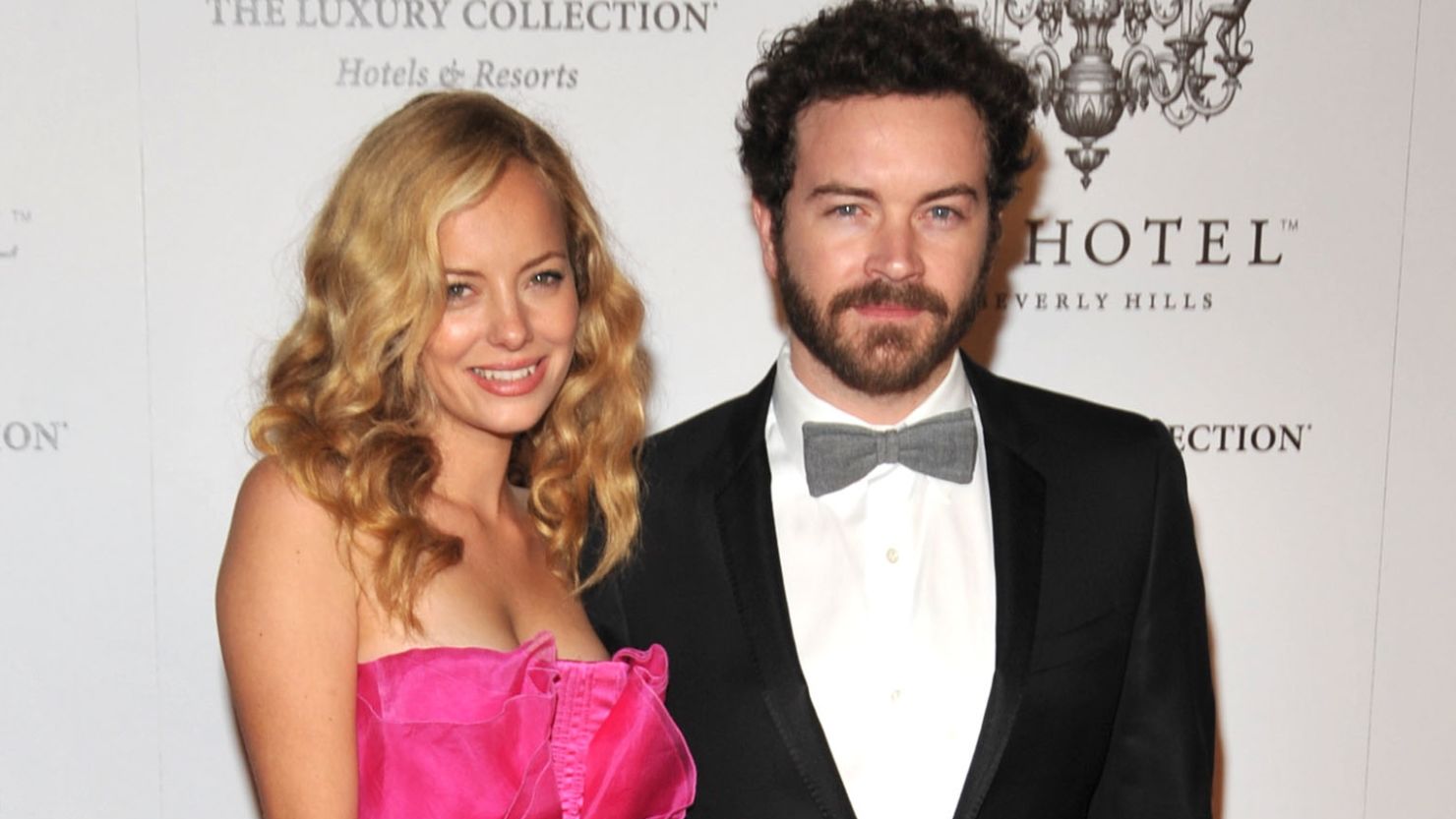 Bijou Phillips and Danny Masterson posing together on a red carpet, with Bijou in a bright pink strapless dress and Masterson in a black tuxedo and bow tie