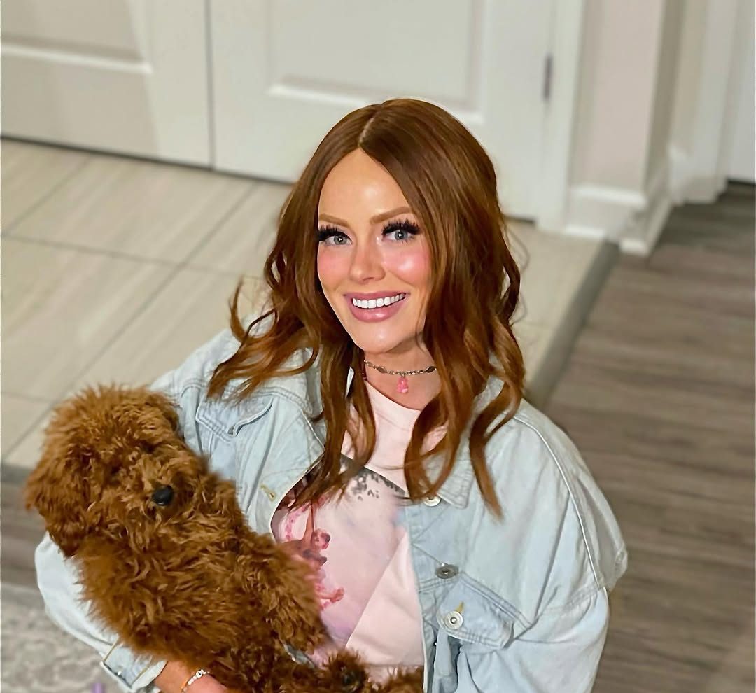 Kathryn Dennis smiling while sitting indoors holding a small brown dog.