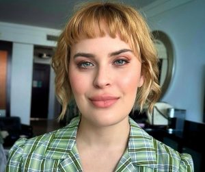 Tallulah Willis poses indoors wearing a green plaid blouse, smiling softly at the camera.