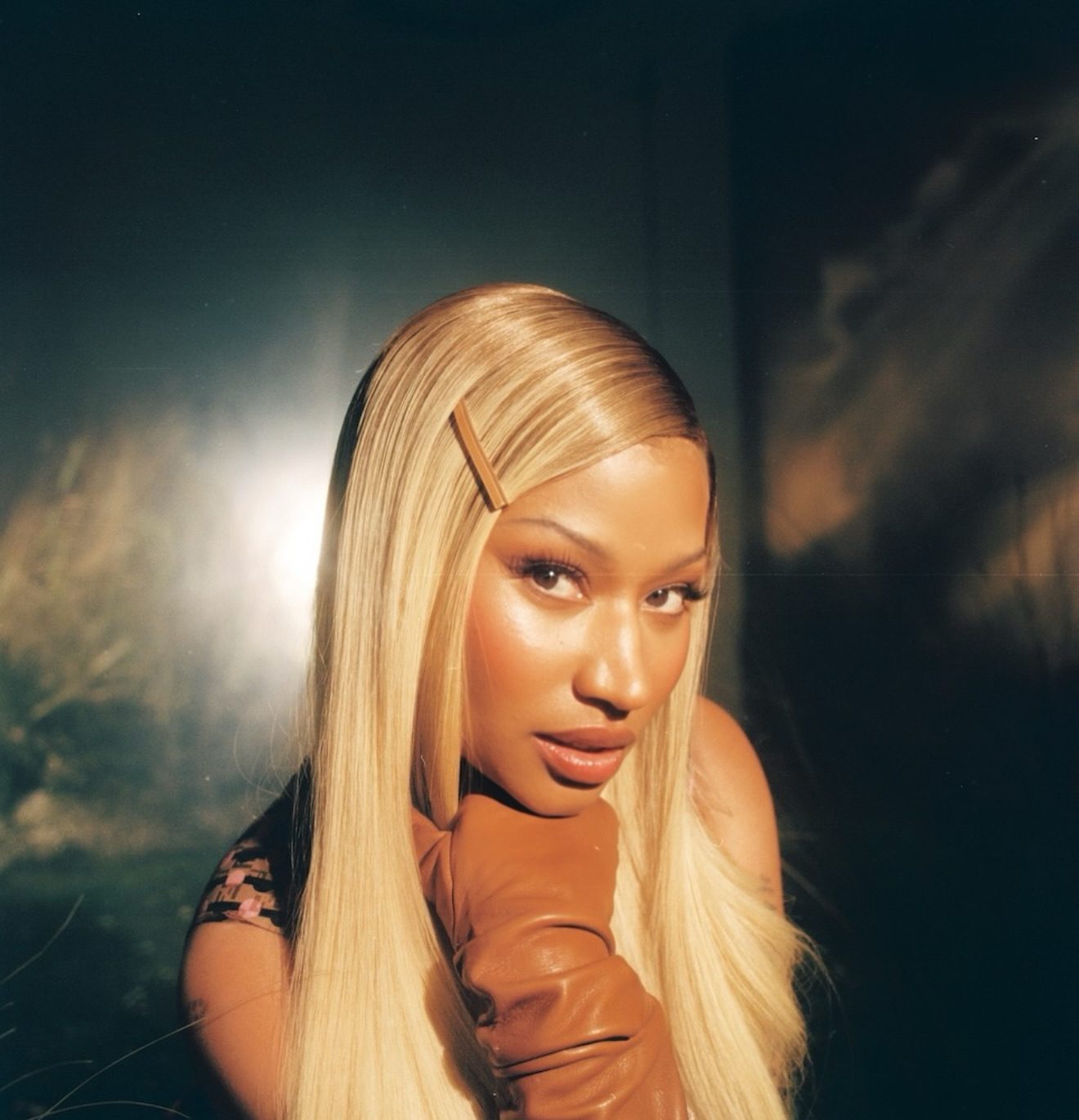 Nicki Minaj poses with long blonde hair, brown gloves, and soft lighting during a photoshoot.