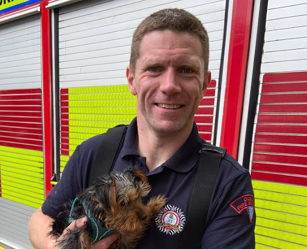 Irish firefighter Terence Crosbie holding a small terrier dog in front of a fire engine.