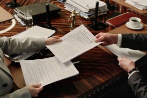 two attorneys exchanging documents sitting side by side at table