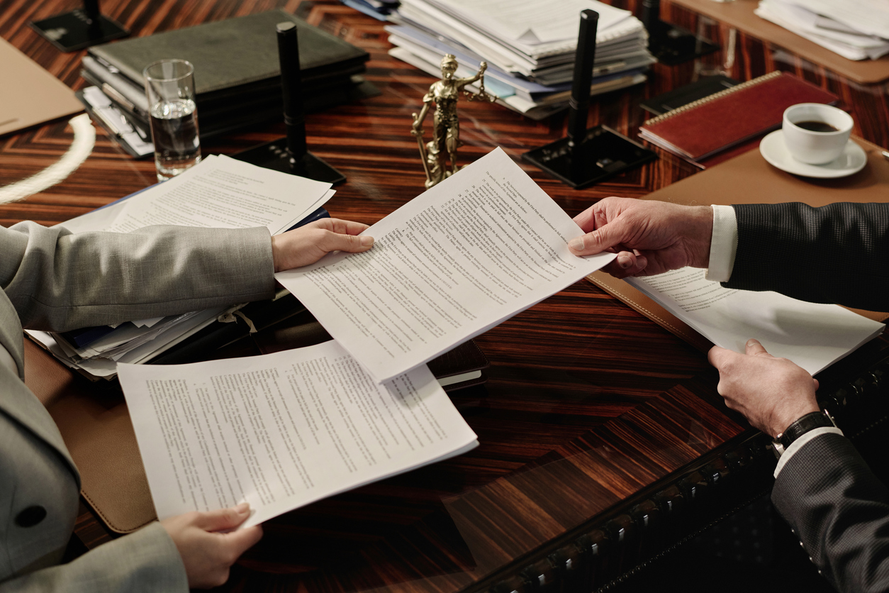 two attorneys exchanging documents sitting side by side at table