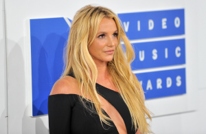 Britney Spears poses on the red carpet at the MTV Video Music Awards, wearing a black off-the-shoulder dress and long blonde hair styled in loose waves.