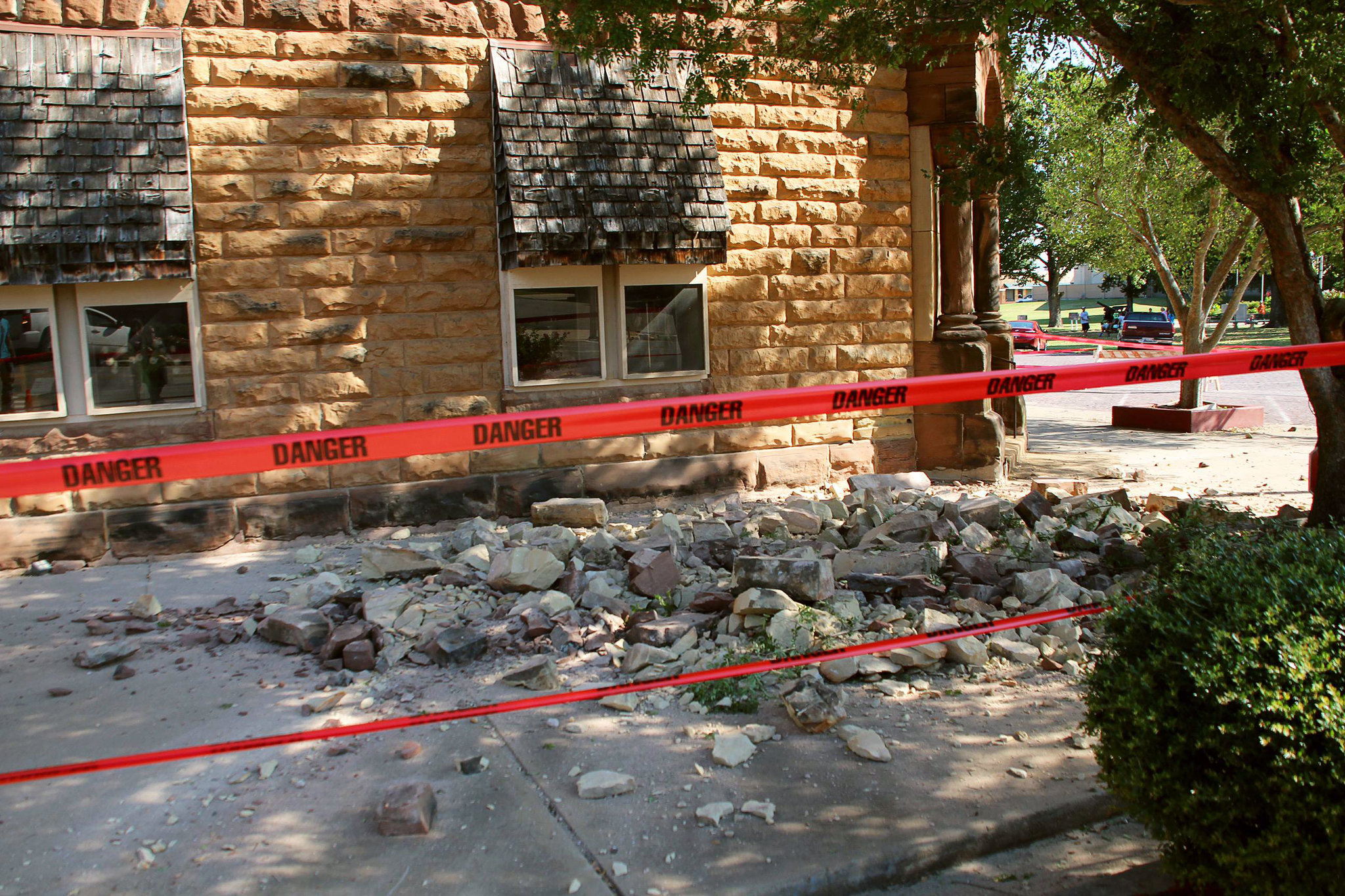 Earthquake damage in Oklahoma showing crumbled stone debris outside a historic building marked with red danger tape after a man-made seismic event.