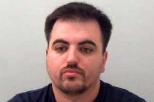Police custody photograph of a man with short dark hair and a trimmed beard, facing the camera against a plain background.
