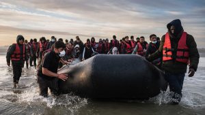 A large group of migrants wearing life jackets push an inflatable dinghy into the sea at dawn as they prepare to cross the English Channel.