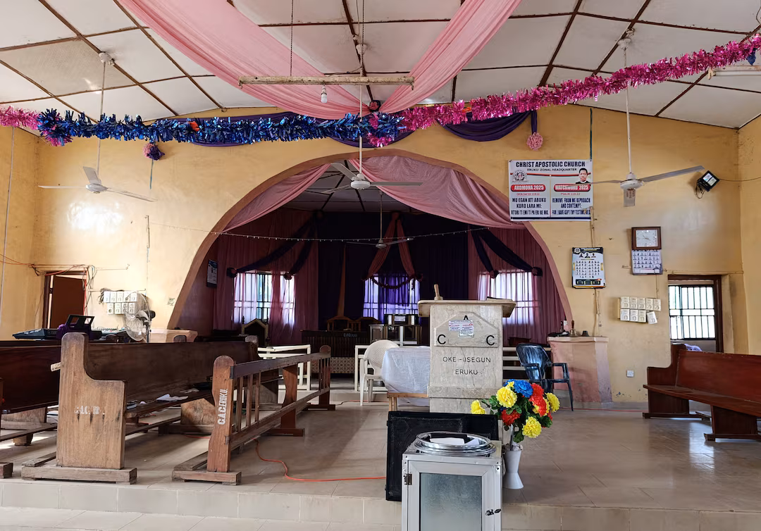 Interior of Christ Apostolic Church in Eruku, Kwara State, showing empty wooden pews, decorated ceiling drapes, and the pulpit after the armed attack.