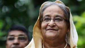 Sheikh Hasina photographed outdoors during a public appearance, wearing a light headscarf and glasses.