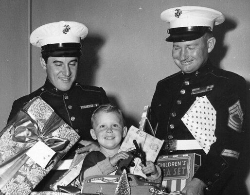 Two U.S. Marines help a young boy place donated Christmas gifts into a Toys for Tots collection bin.