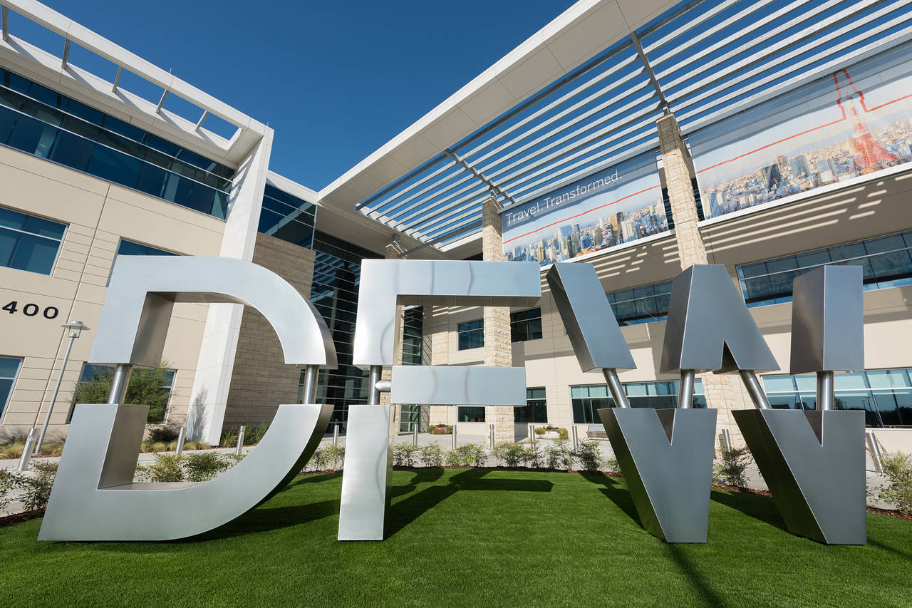 Large silver “DFW” letters in front of the main terminal building at Dallas–Fort Worth International Airport on a sunny day, symbolizing Texas air travel.