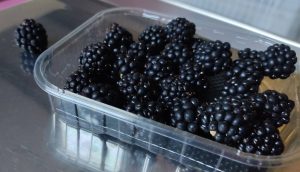 Fresh blackberries in a clear plastic produce container on a reflective surface.