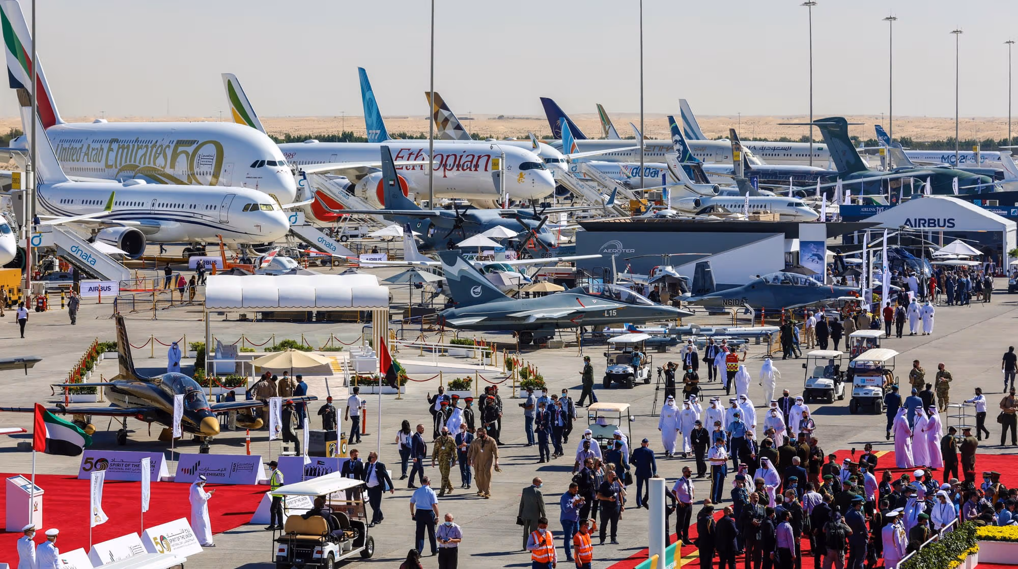 Crowds and aircraft on display at the Dubai Air Show, featuring commercial jets, military aircraft, and exhibition stands across the airfield.