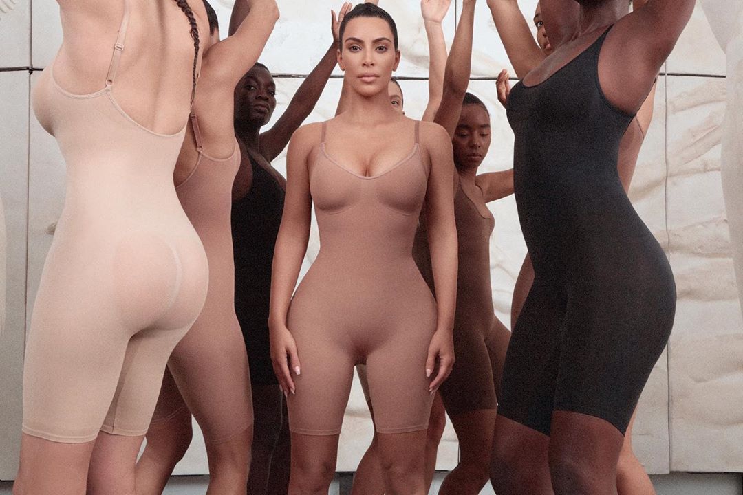 Kim Kardashian standing in the center wearing Skims shapewear, surrounded by models in different skin-tone bodysuits.