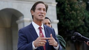 Los Angeles County District Attorney Nathan Hochman speaking at a press conference, gesturing with his hands while addressing reporters outside a government building.