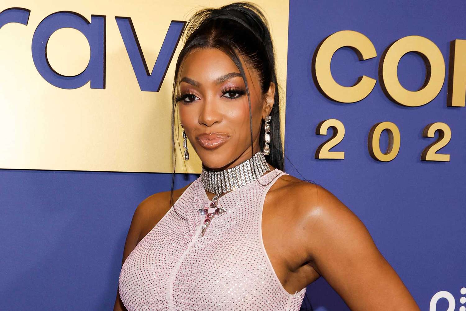 Porsha Williams posing on the BravoCon 2025 red carpet in a pink rhinestone halter dress
