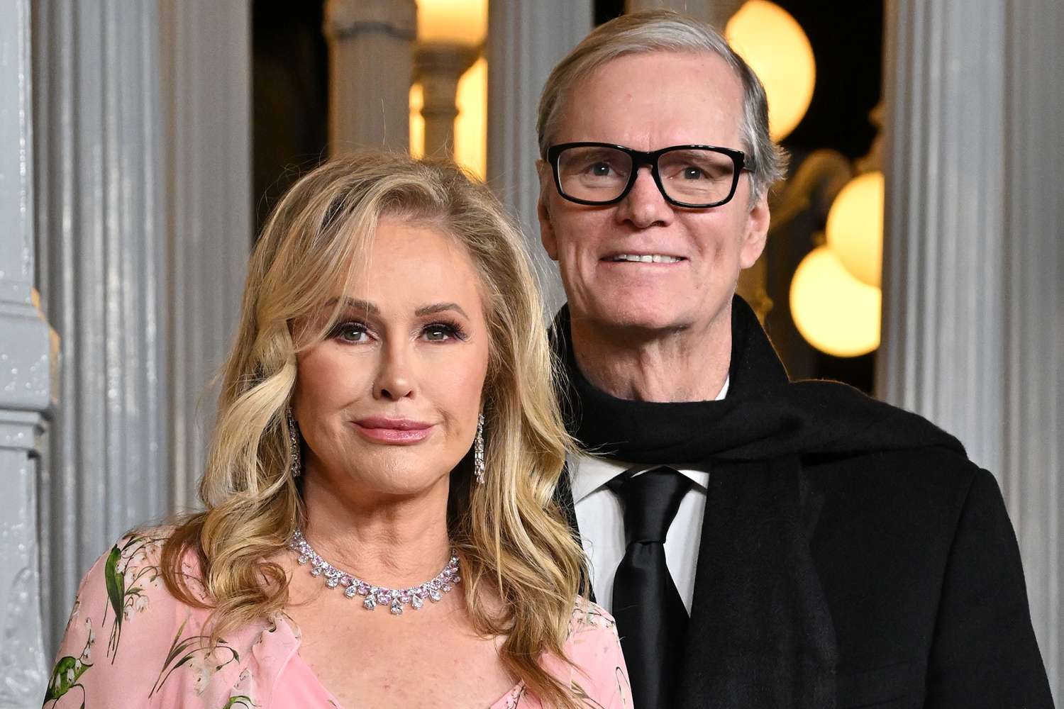 Kathy Hilton standing beside her husband Rick Hilton at an event, both dressed formally with decorative lighting in the background.