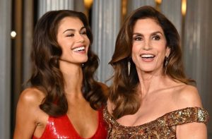 Kaia Gerber in a red sequined dress and Cindy Crawford in a gold sequined off-the-shoulder dress smiling at an event.