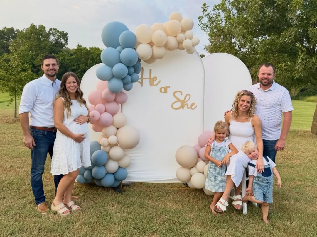 Jana and John-David Duggar with their spouses and children at a joint gender reveal party featuring a “He or She” balloon display outdoors.