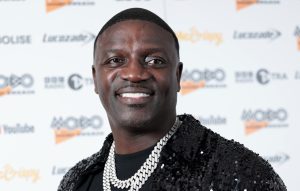 Akon attends the MOBO Awards in London wearing a black sequined jacket and diamond chain, smiling on the red carpet.
