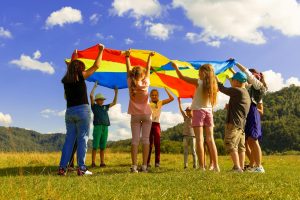 Children playing with a colourful parachute outdoors during a summer camp activity.