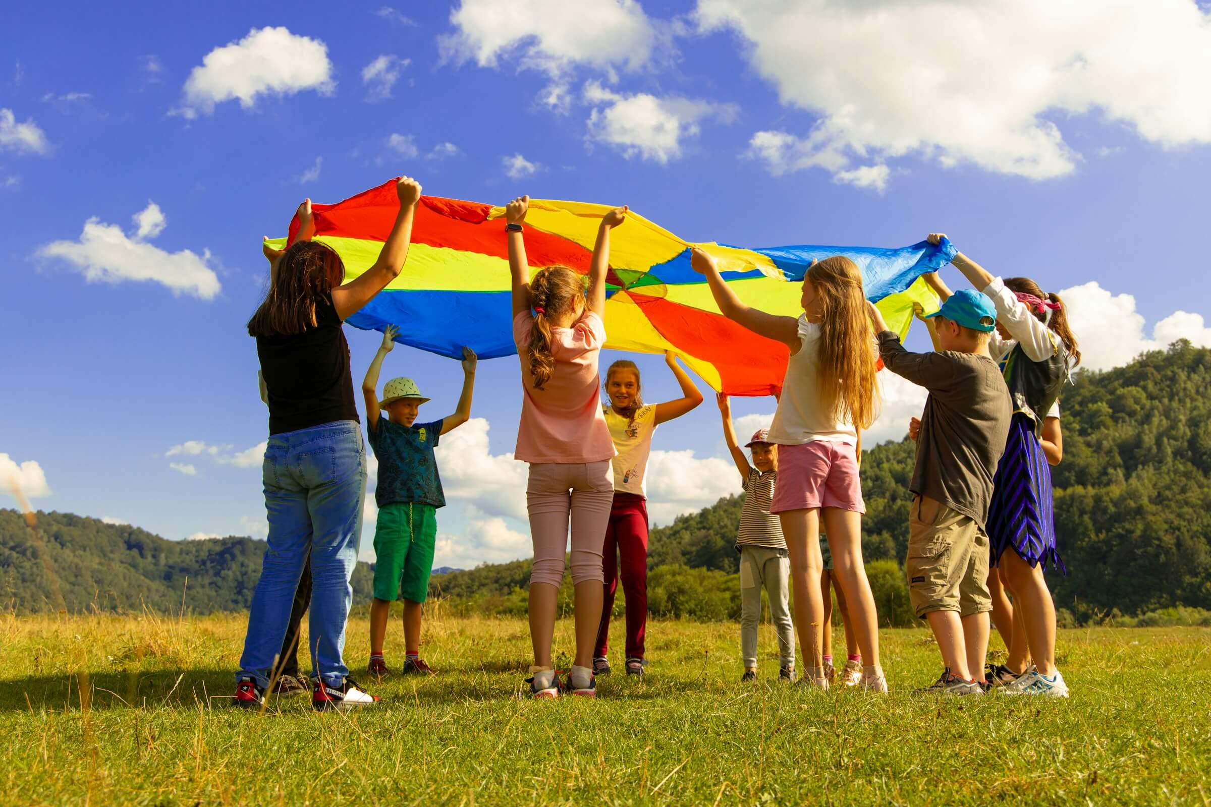 Children playing with a colourful parachute outdoors during a summer camp activity.