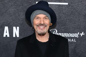 Headshot of actor Billy Bob Thornton wearing a navy fedora over a grey beanie, smiling.