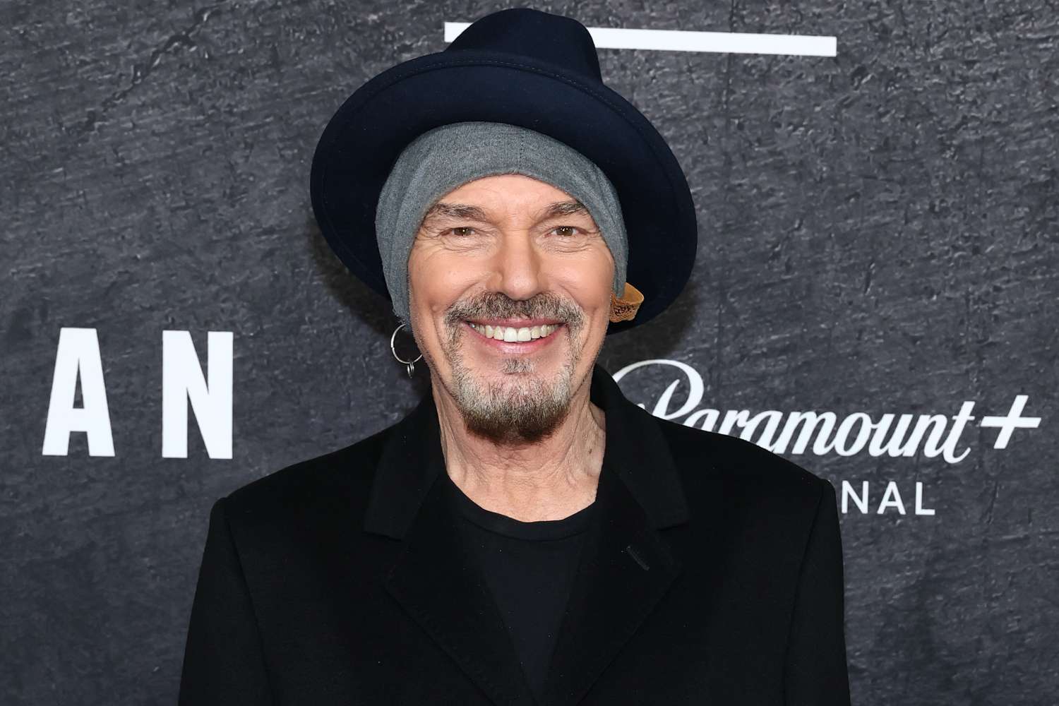 Headshot of actor Billy Bob Thornton wearing a navy fedora over a grey beanie, smiling.