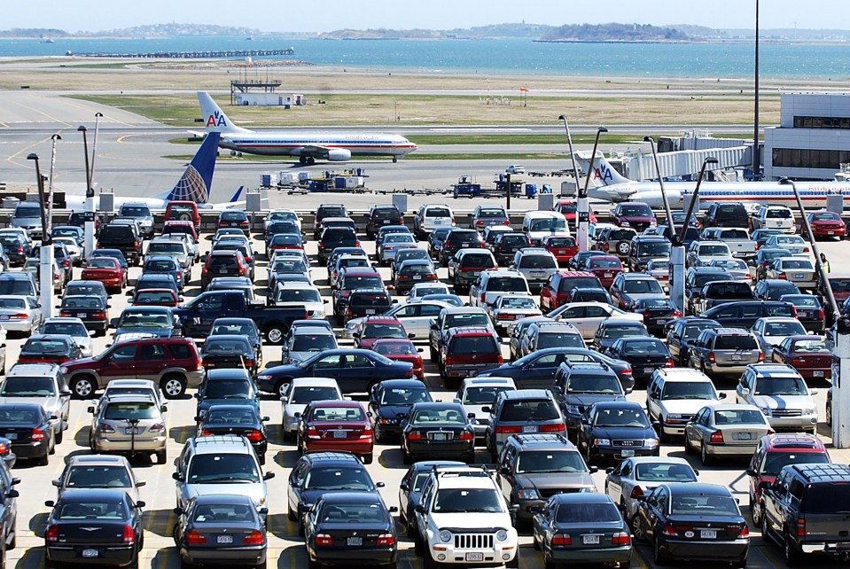 Crowded parking lot at Boston Logan Airport with rows of parked cars and airplanes taxiing on the runway in the background.