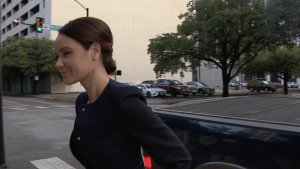 Stephanie Hockridge walking outside near a street intersection, wearing a dark outfit and appearing to enter a building.