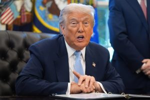 President Donald Trump speaks during an Oval Office meeting, seated at a desk with documents in front of him.