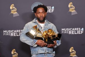 Kendrick Lamar holding multiple GRAMMY Awards at a MusiCares Fire Relief event, symbolizing his success and growing influence in the music industry’s legal ownership movement.