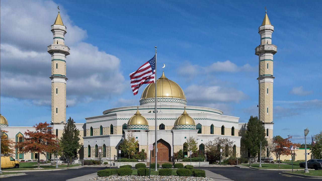 The Islamic Center of America in Dearborn, Michigan, with its gold domes and twin minarets, seen under a clear sky with an American flag in front.